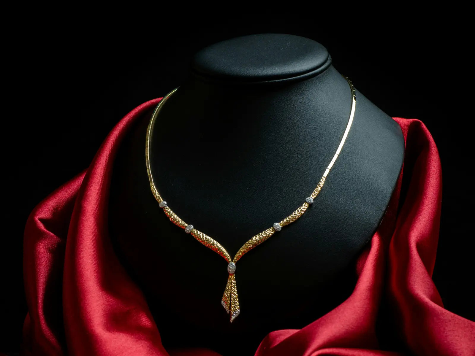 An intricate gold necklace displayed on a dark stand with rich red satin — representing the essence of true luxury where craftsmanship and beauty speak louder than price